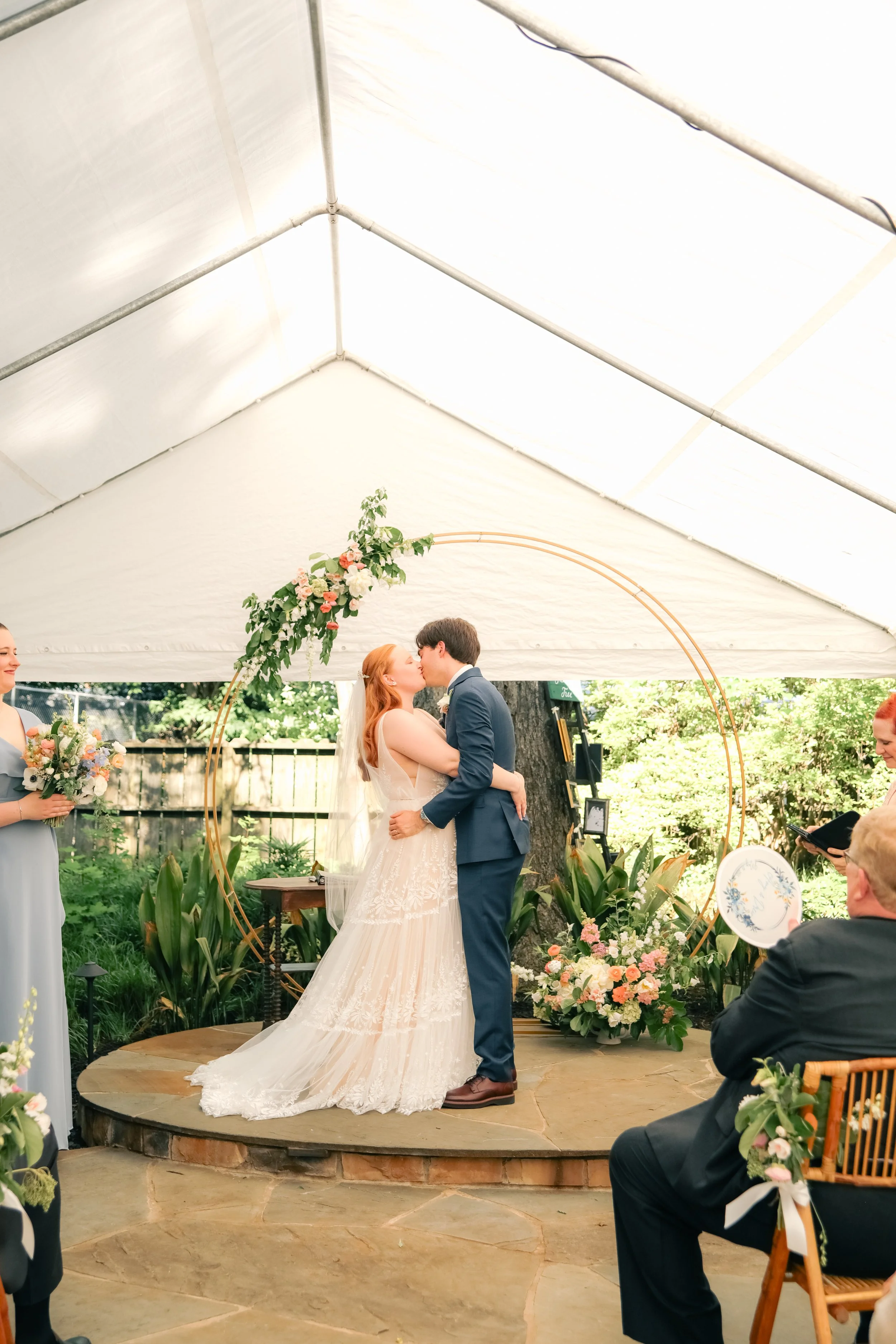 Newlyweds kiss beneath a pink and peach spring wedding arch at the Rosemary House Inn in Pittsboro, NC