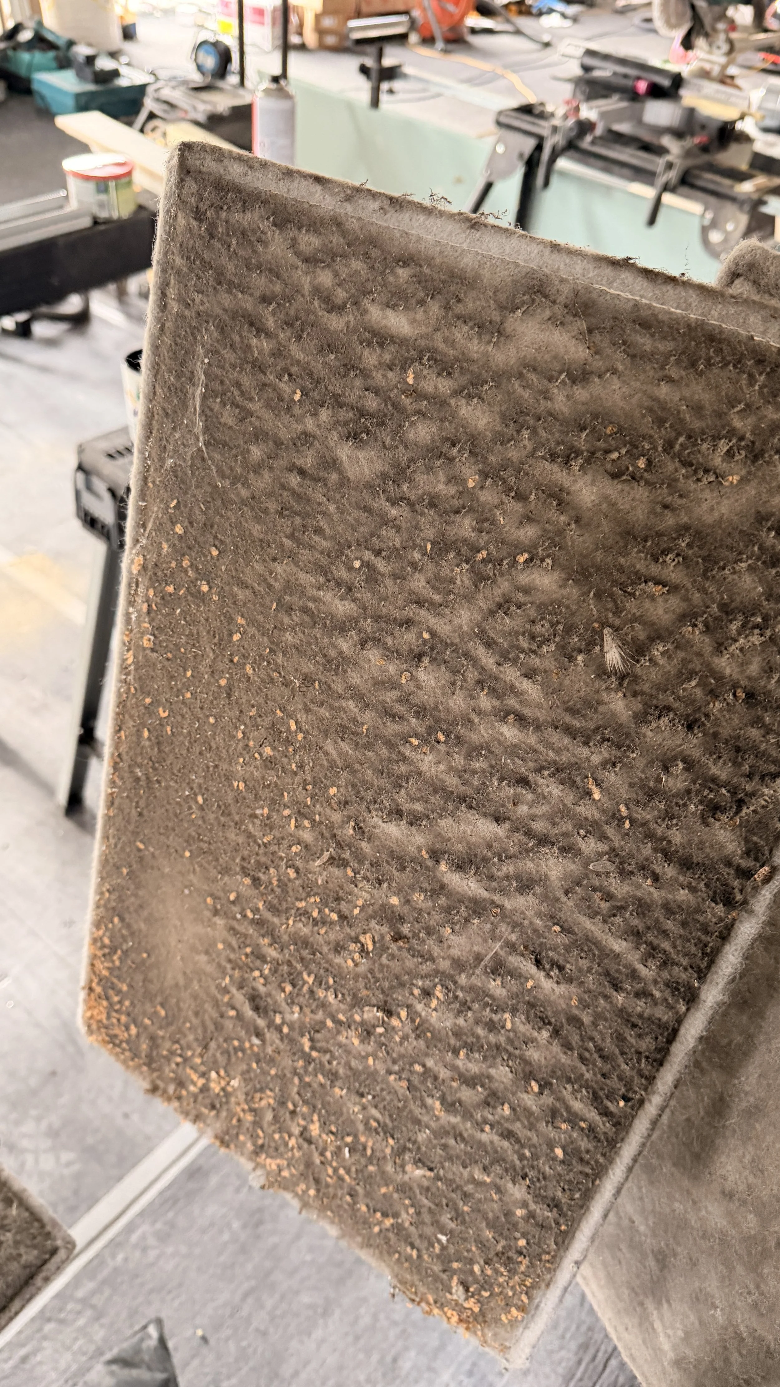 Close-up of a dirty, used air filter with dust and debris visible on the surface, in a workshop or garage setting.