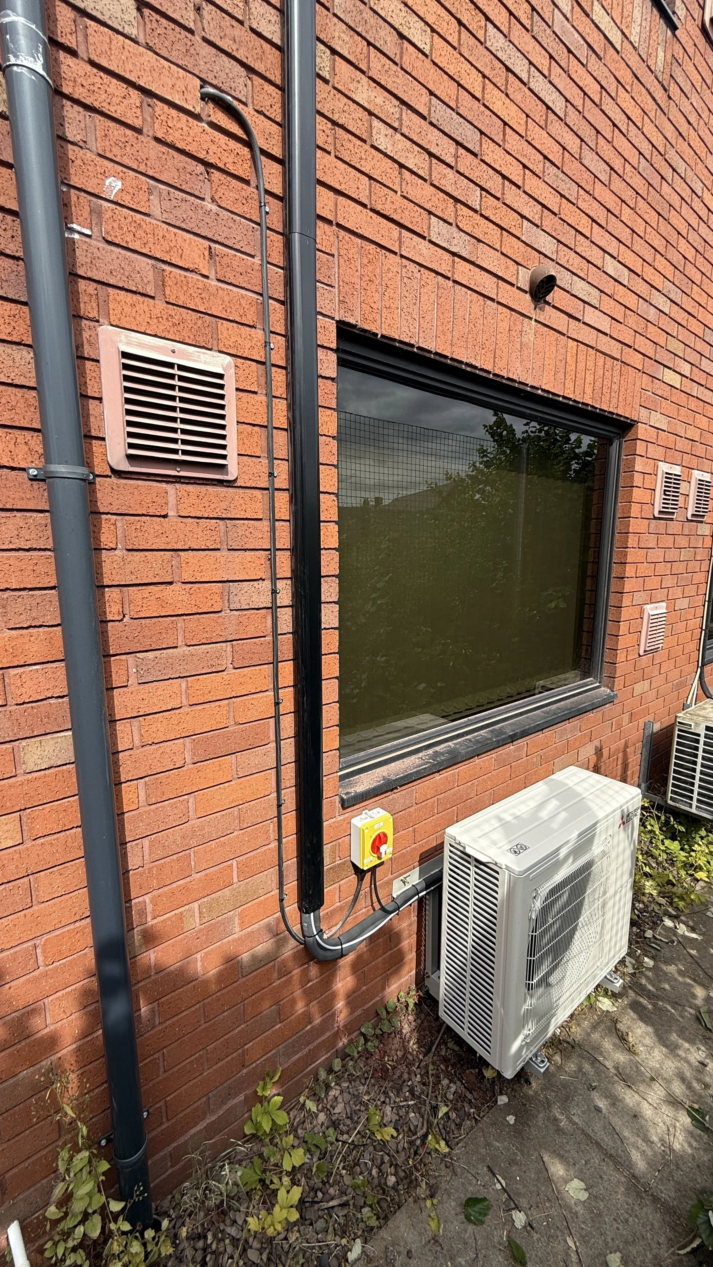 Exterior of a brick building with a window, air conditioning units, and electrical wiring.