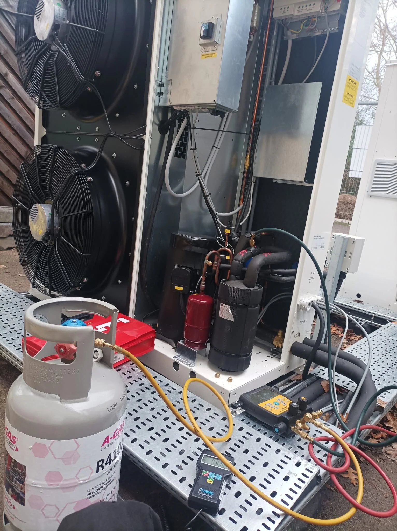 An HVAC unit with various components, including fans, pipes, and electronic controls, is being serviced outdoors. A fire extinguisher and testing tools are nearby.