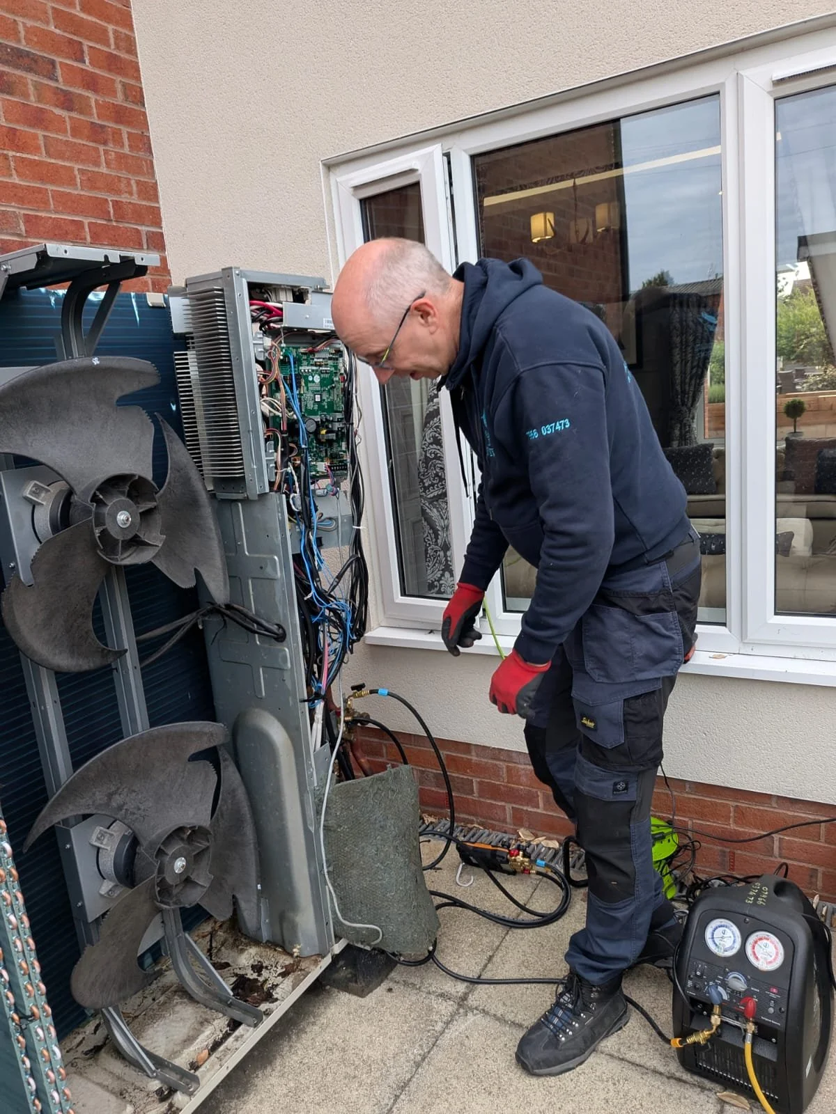 Technician. from Kalmair Ltd wearing a uniform repairing an outdoor air conditioning unit, working with tools and monitoring gauges