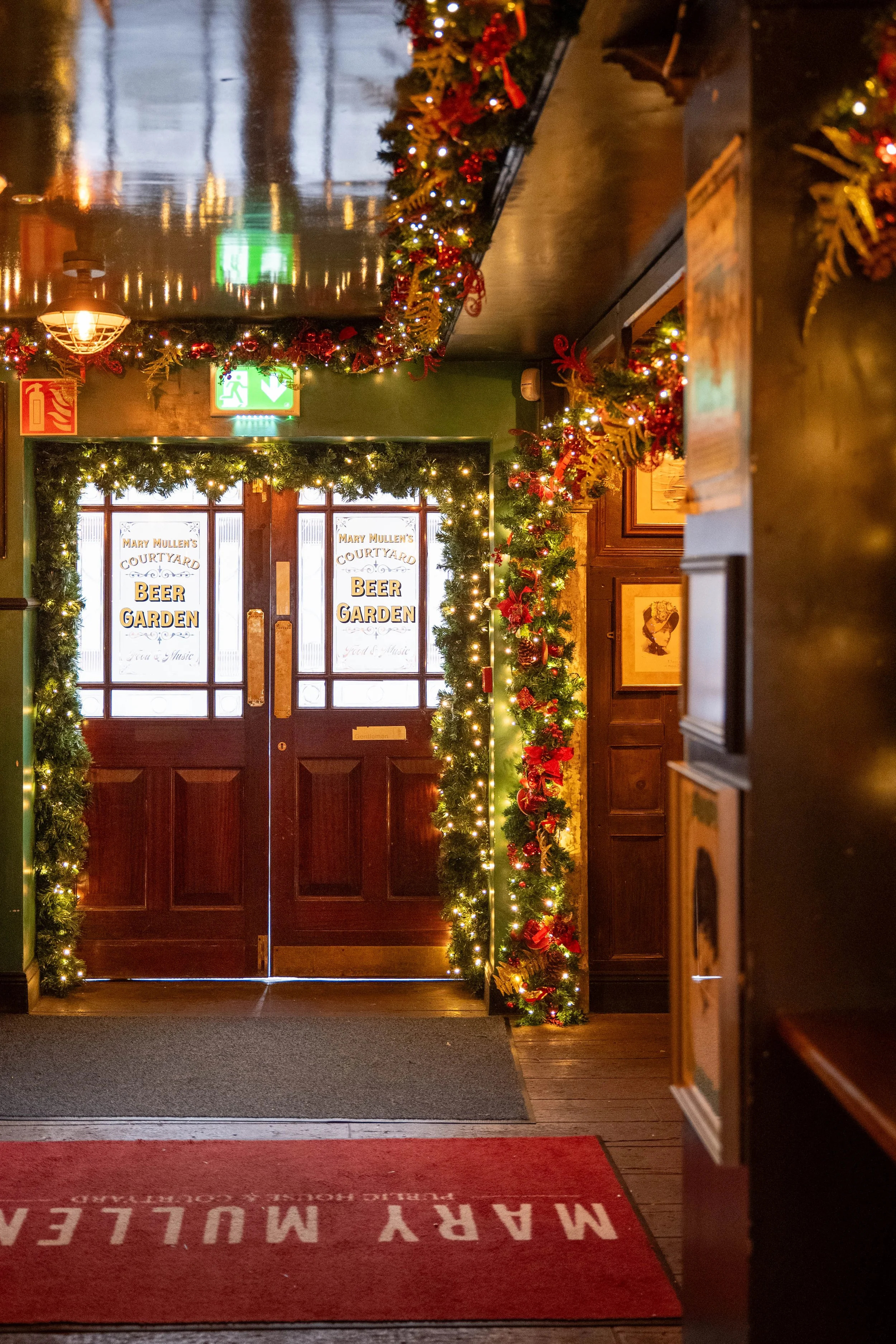 Entrance to Mary Mullen's Courtyard with Christmas decorations, including garlands and fairy lights, framing a wooden door with signs for 'Beer Garden'.