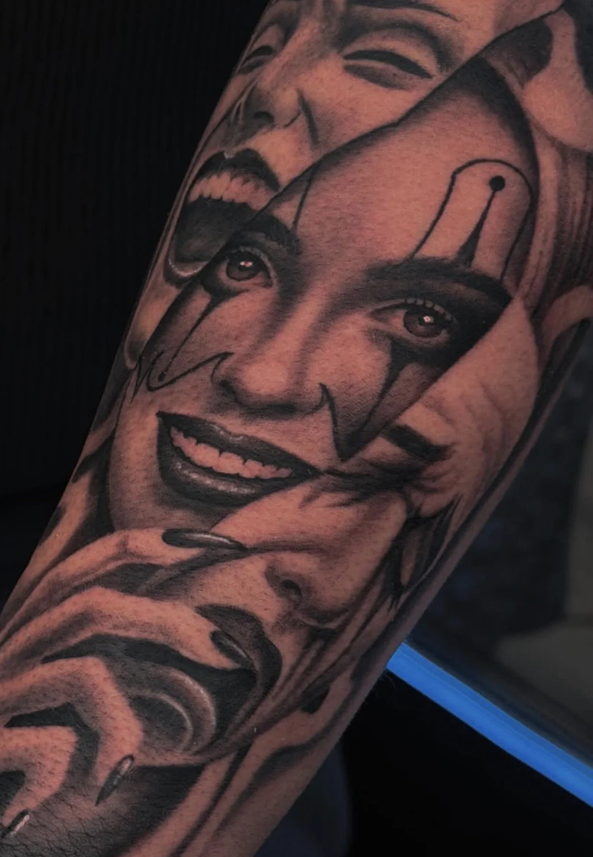 Tattoo of a smiling clown face with makeup and a hat on a person's arm.