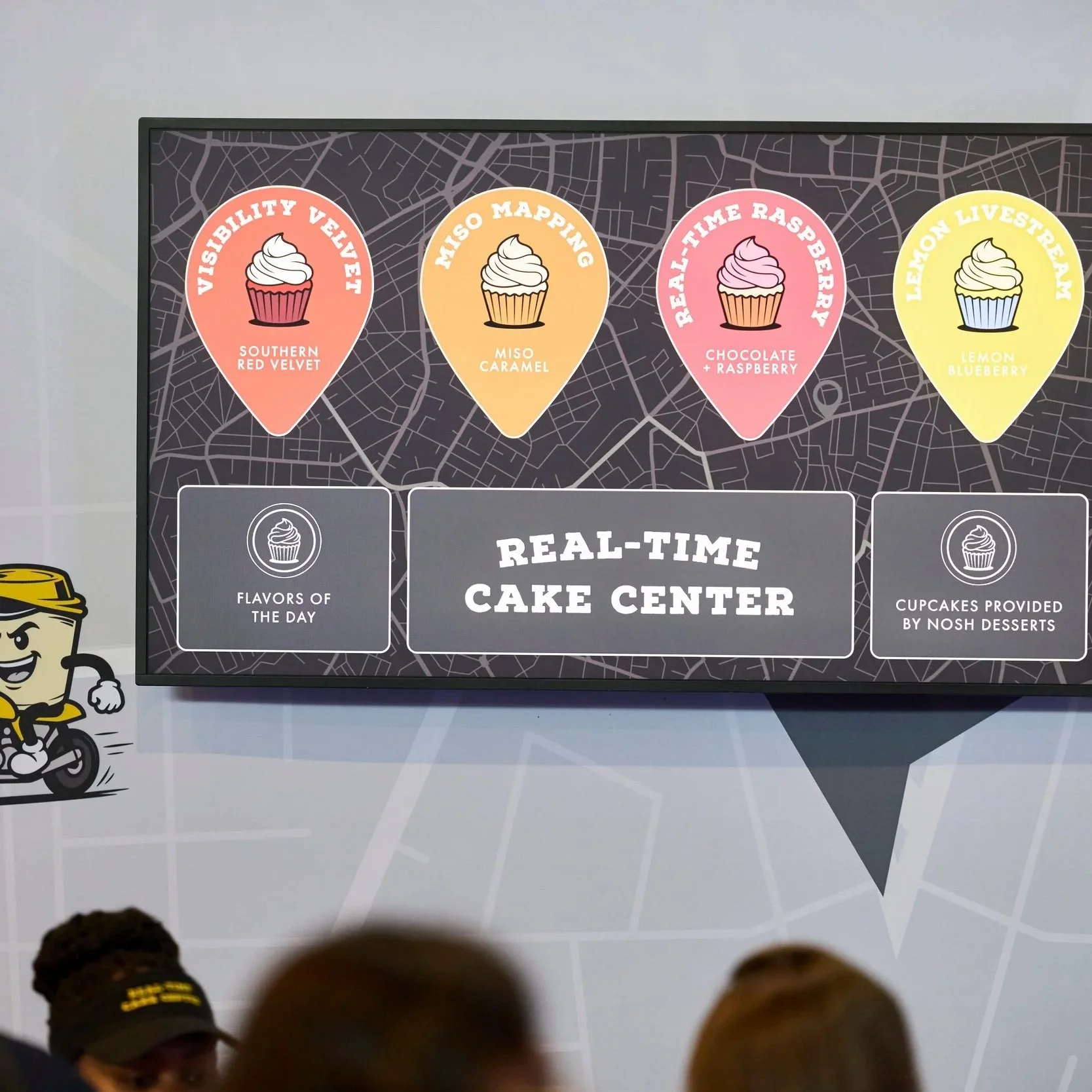 Display screen showing four cupcake flavor options: Southern Red Velvet, Miso Caramel, Chocolate + Raspberry, and Lemon Blueberry, with a background map design.