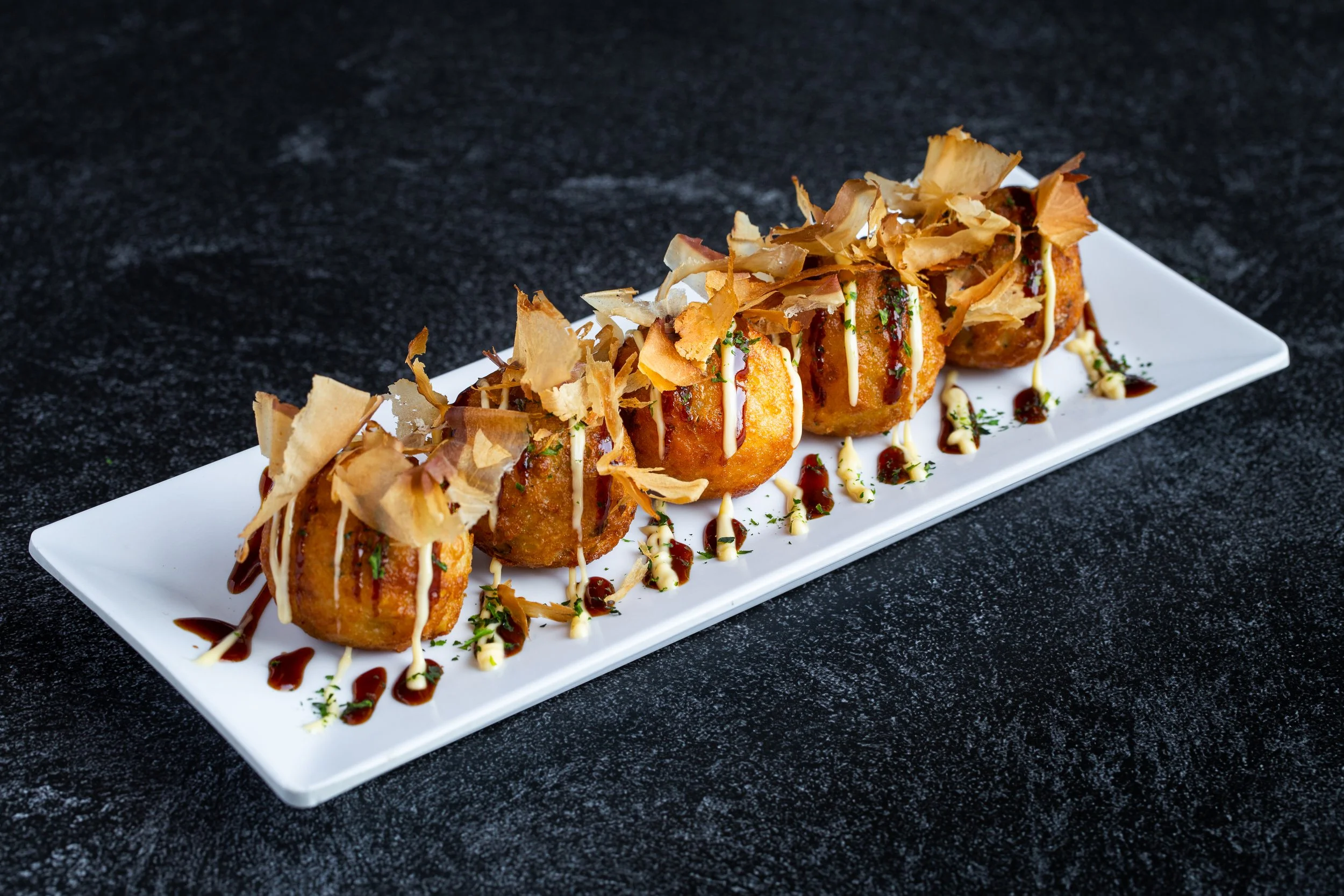 Takoyaki with bonito flakes and green onion on a white plate
