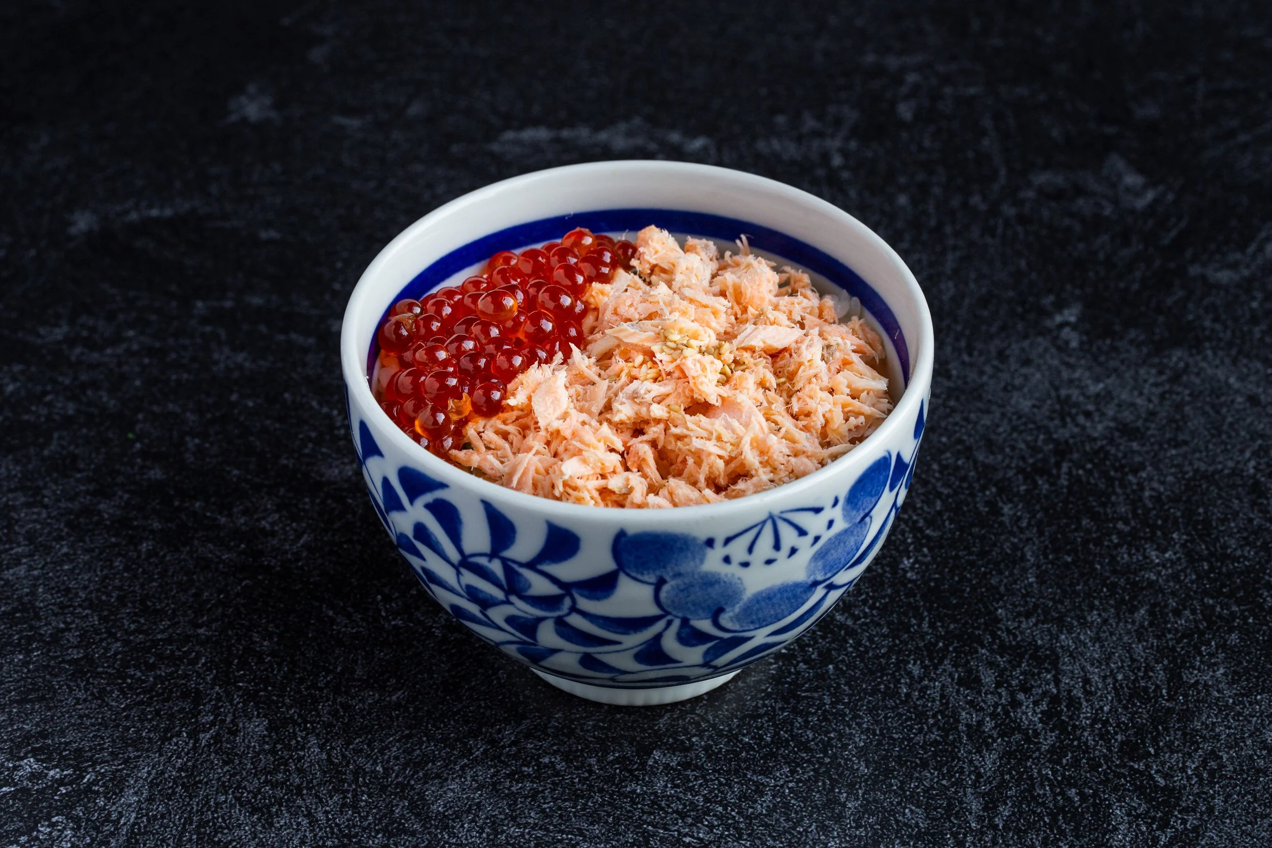 A bowl of rice covered with grilled salmon and salmon roe, topped with dry seaweed