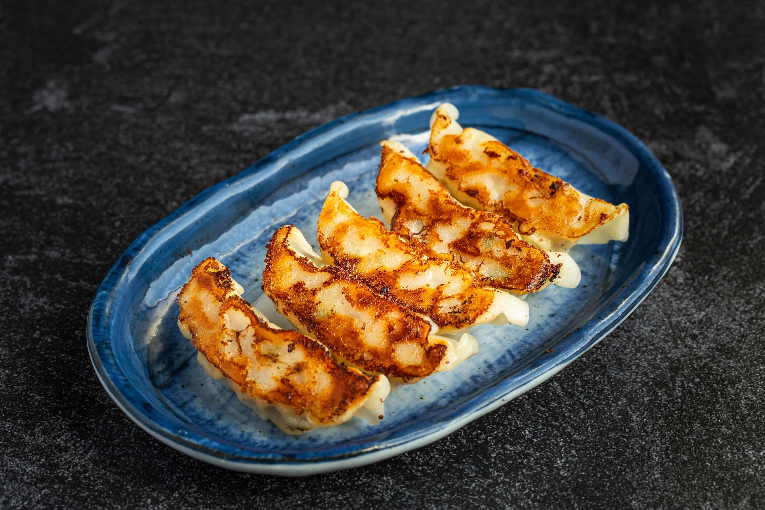 5 pieces of gyoza on a blue plate with a dipping sauce next to it