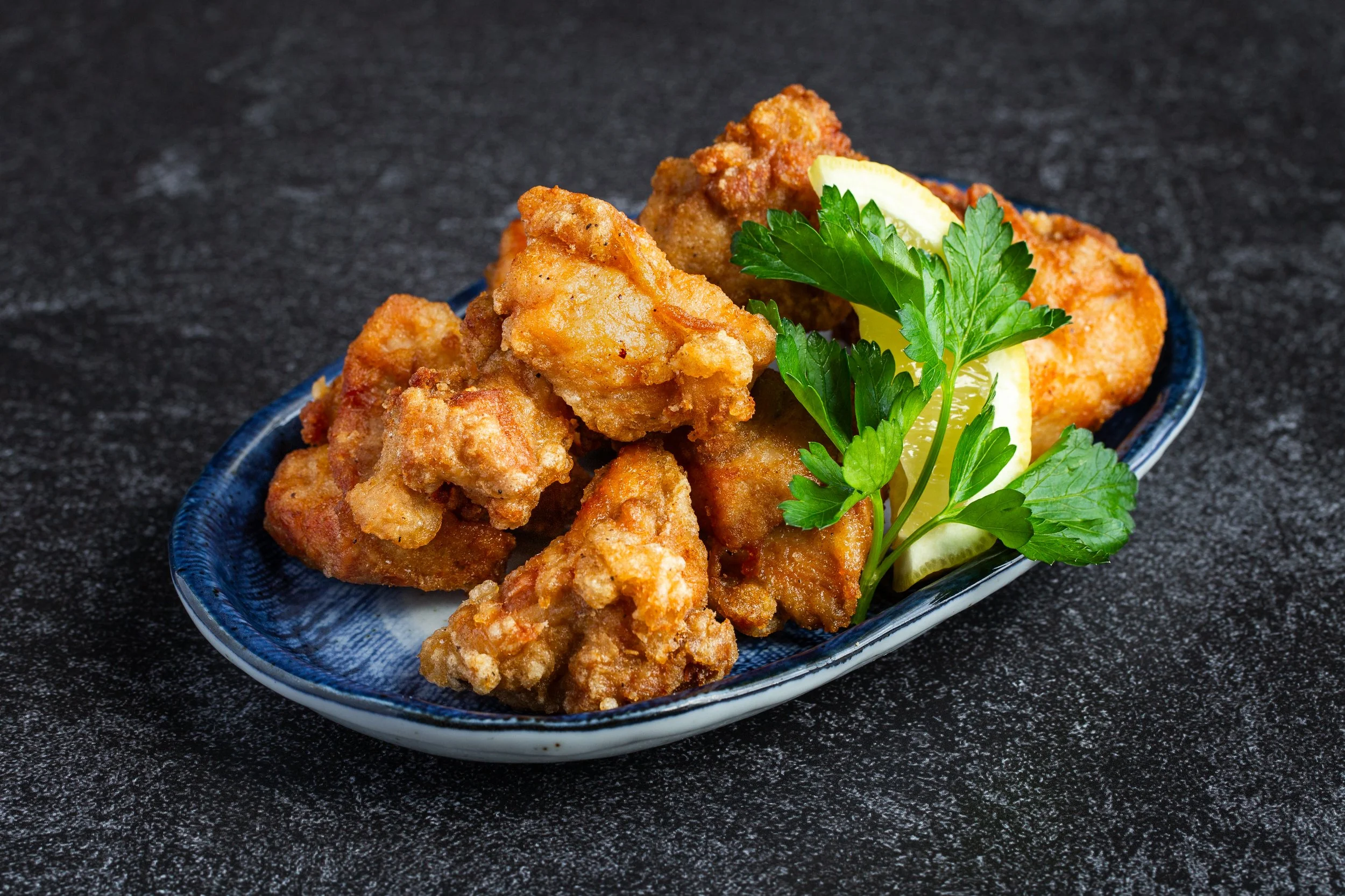 Karaage with lemon wedge and parsley on a blue plate