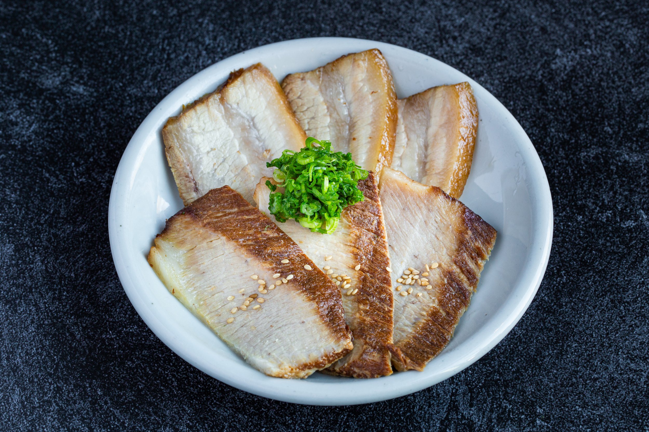 Slices of toro cha-siu with green onions on a plate