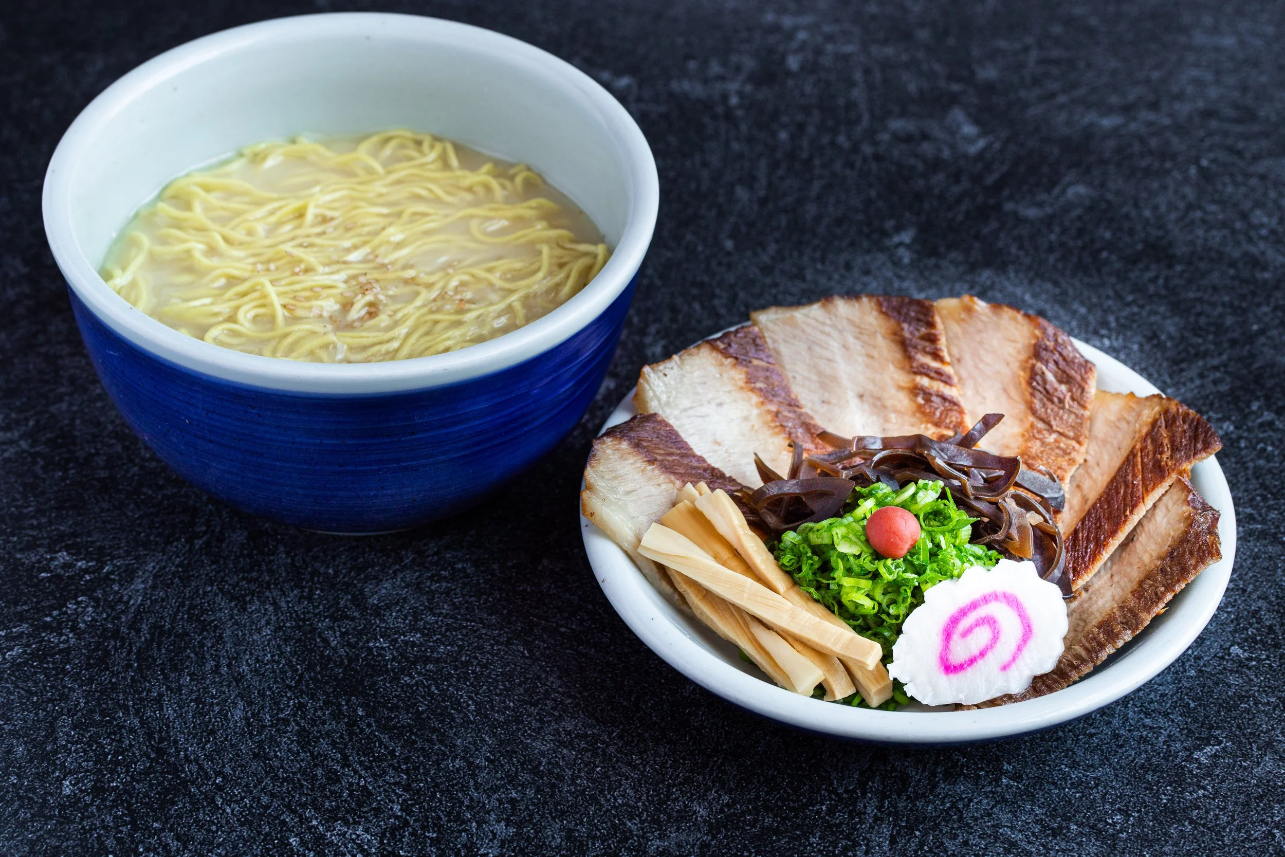 A bowl of ramen with soup, toro-niku, naruto, etc. on a separate plate