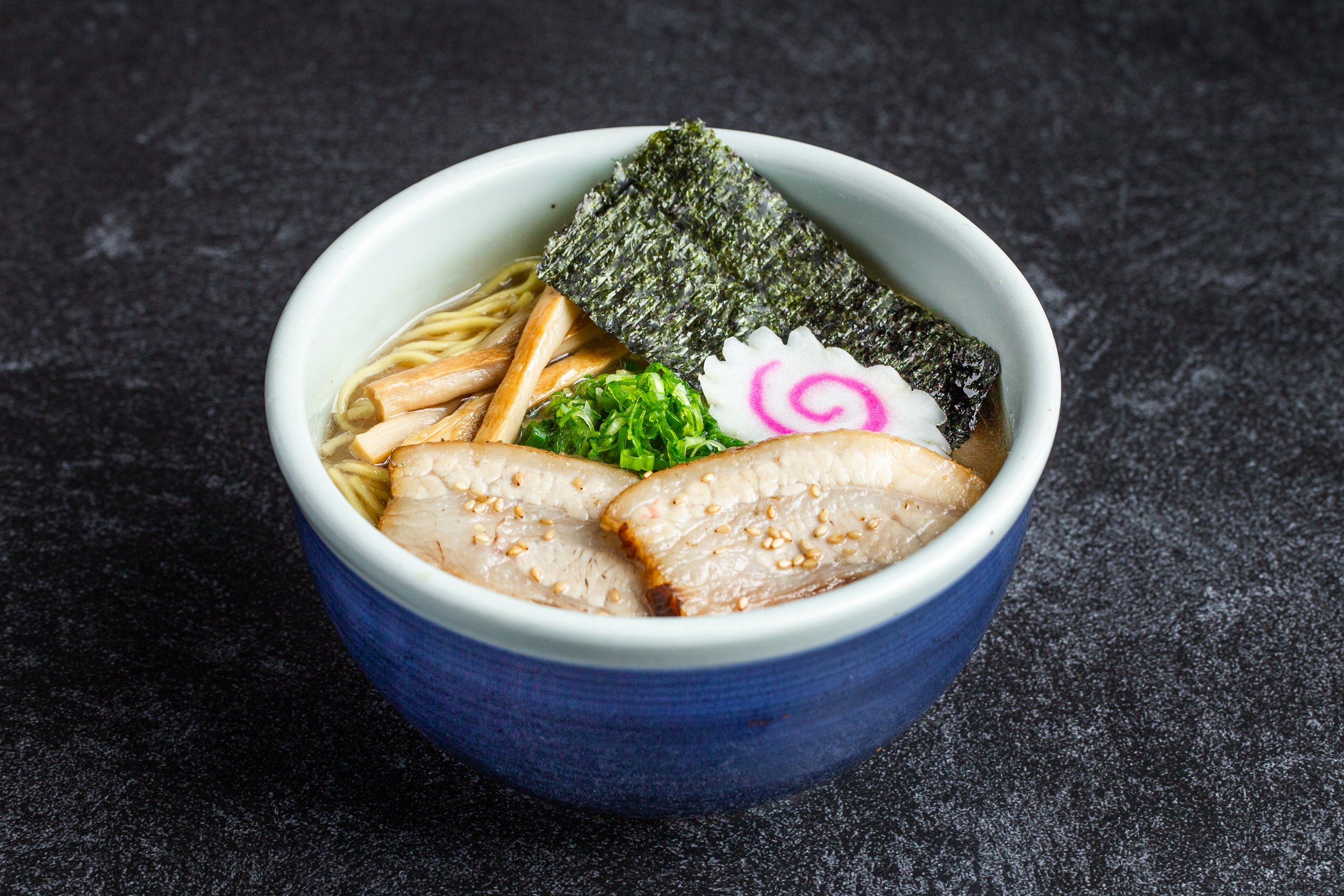 A bowl of shoyu ramen with cha-siu along with naruto, green onions, seaweed, etc.