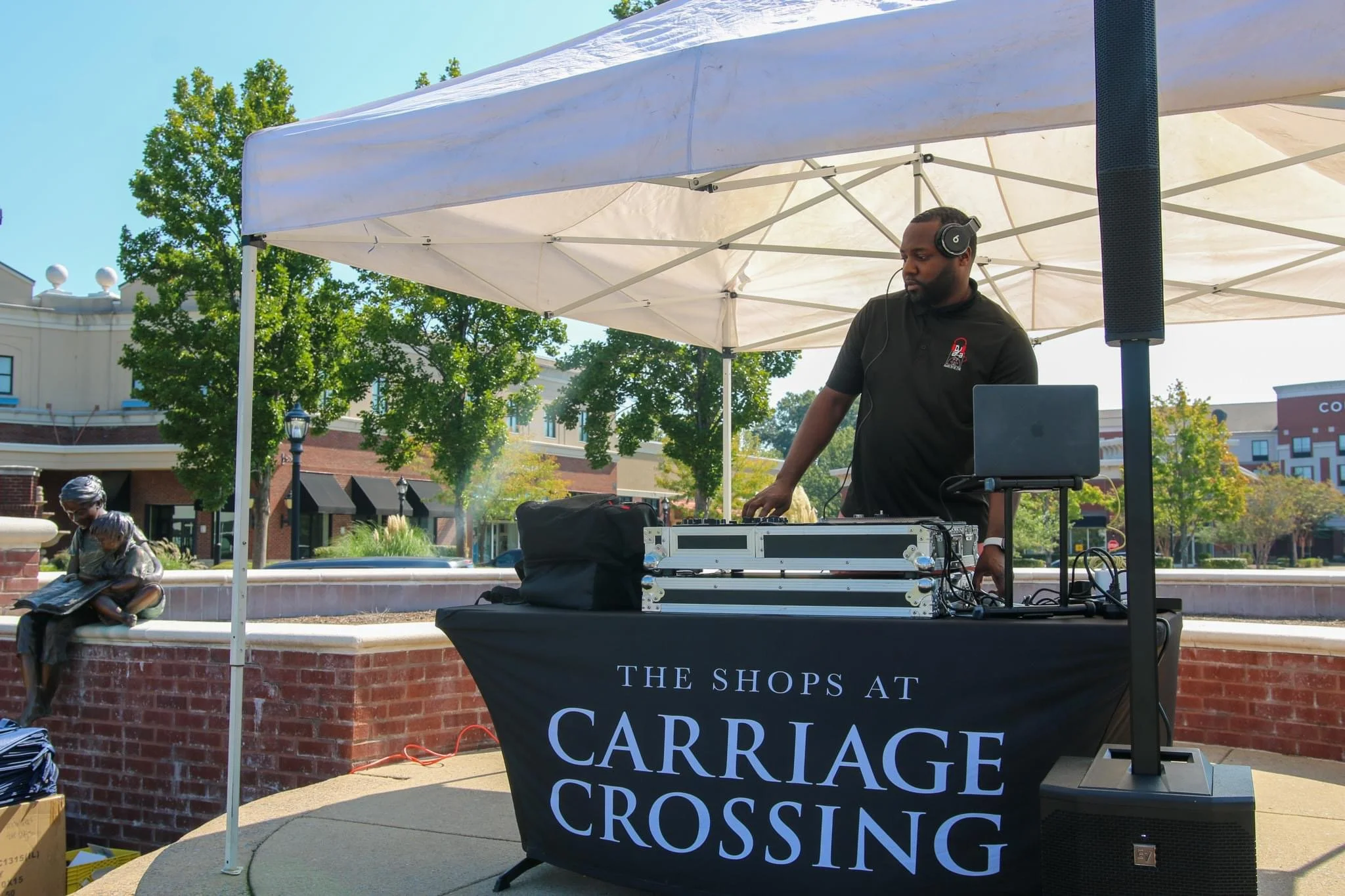 A man wearing headphones DJing at an outdoor event beneath a white canopy, Carriage Crossing DJ