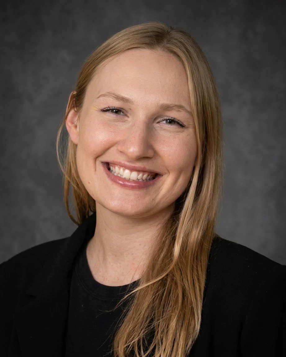 Therapist in Flint MI Julia Teper: A professional psychologist who is smiling. She is wearing a black long sleeve shirt. The background is a textured grey.