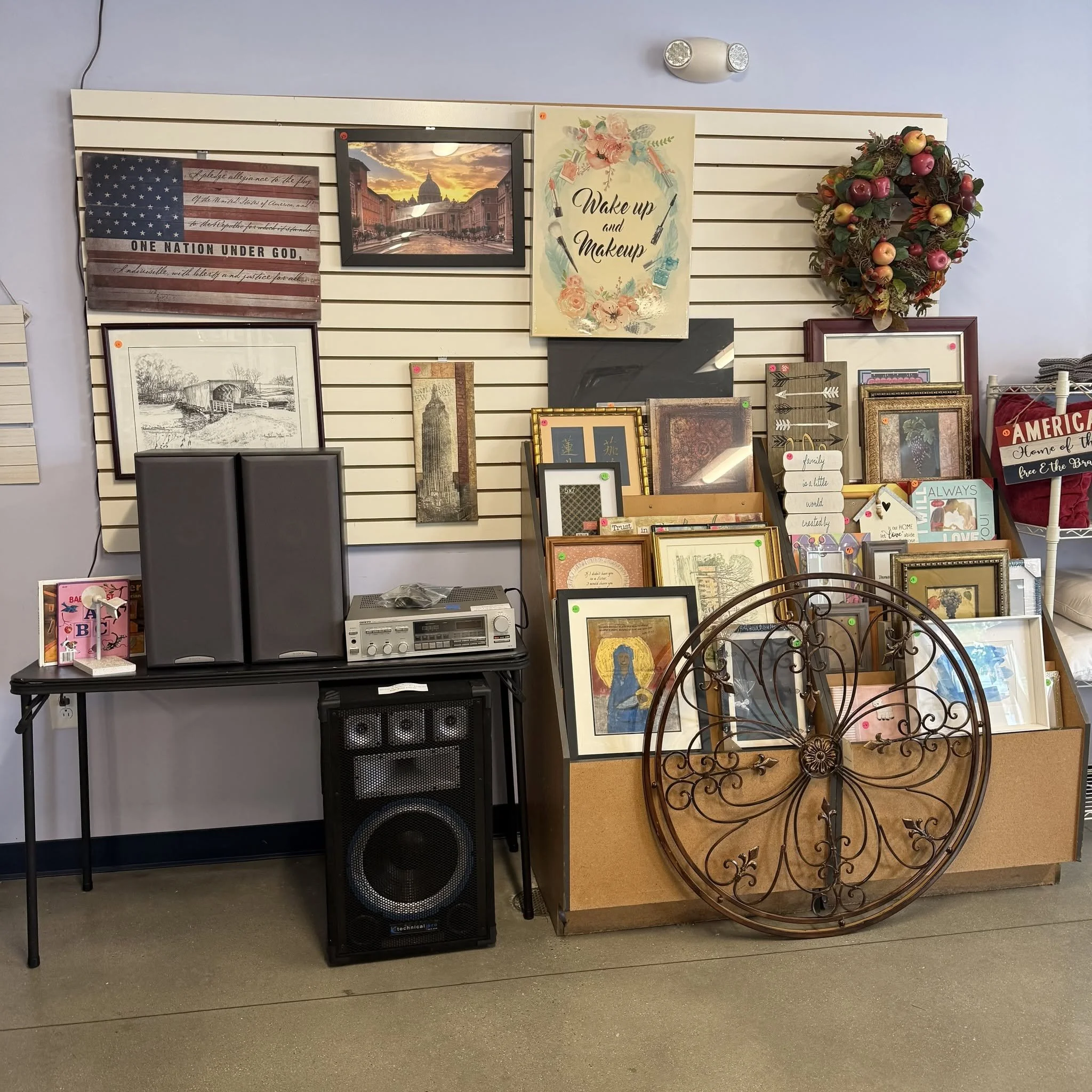 Display of framed pictures, wall décor, and floral wreath on a slatwall in a store.