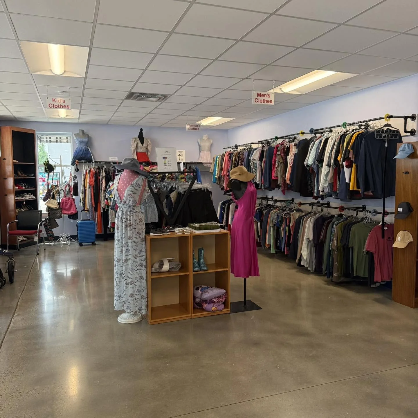 Clothing store interior with racks of women's, men's, and kids' clothes, and mannequins wearing dresses.