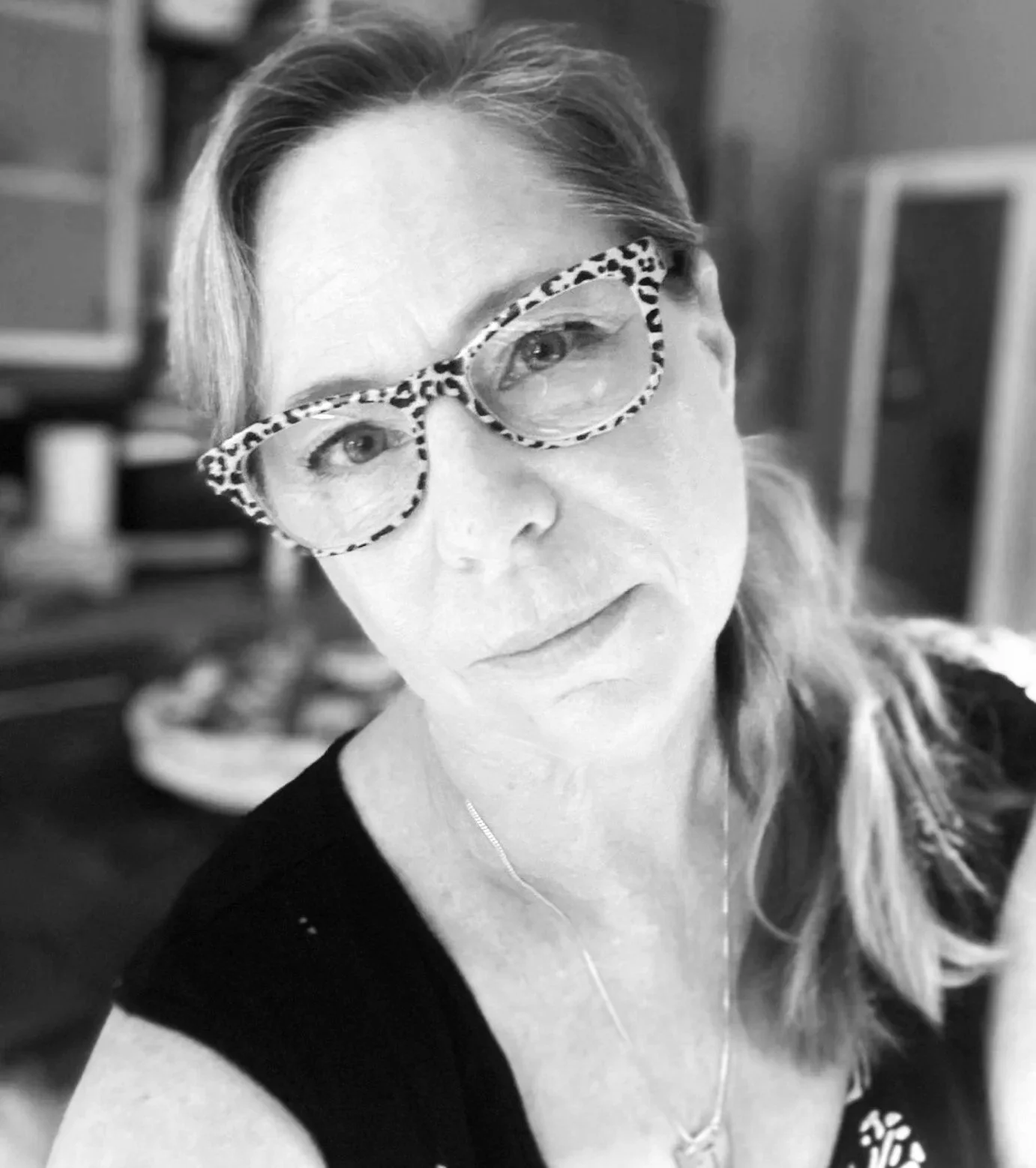 A close-up black and white photo of Jacquie Court wearing leopard print glasses, with light-colored hair, looking into the camera.