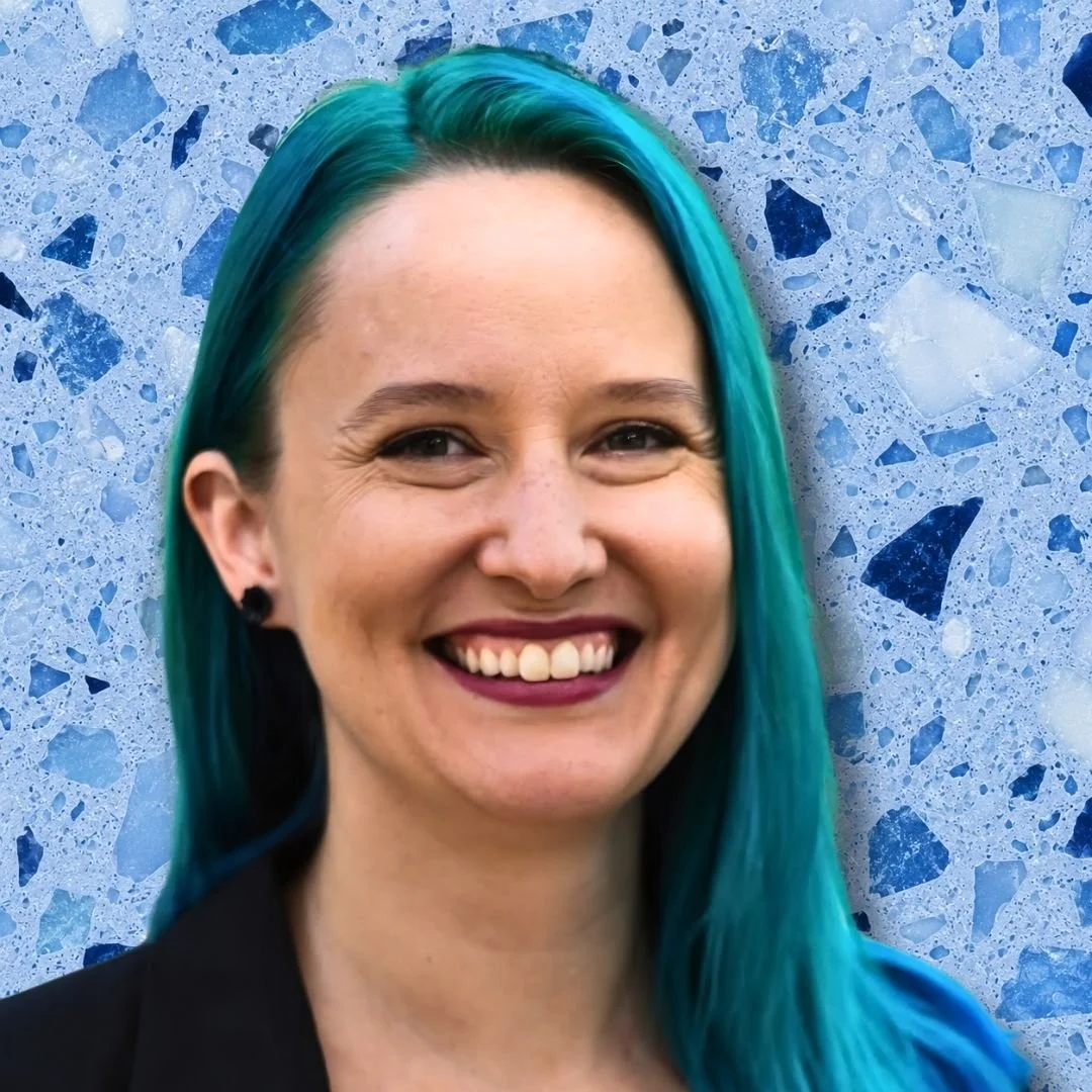 A woman with blue-green hair smiling against a blue terrazzo background.