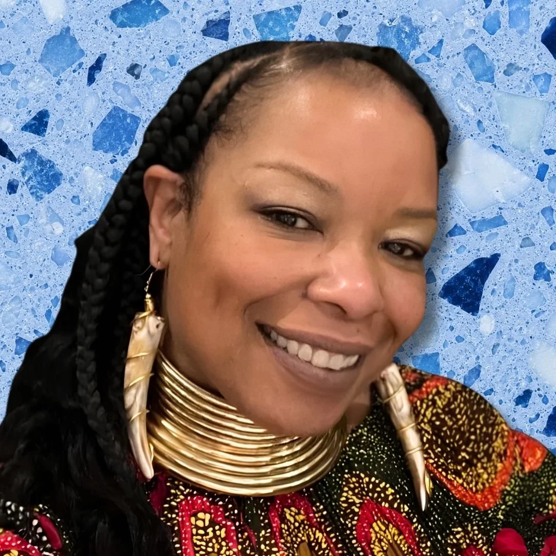 A woman smiling, wearing traditional Maasai jewelry including stacked gold necklaces, large earrings, and a colorful patterned cloth, with a blue marble background.