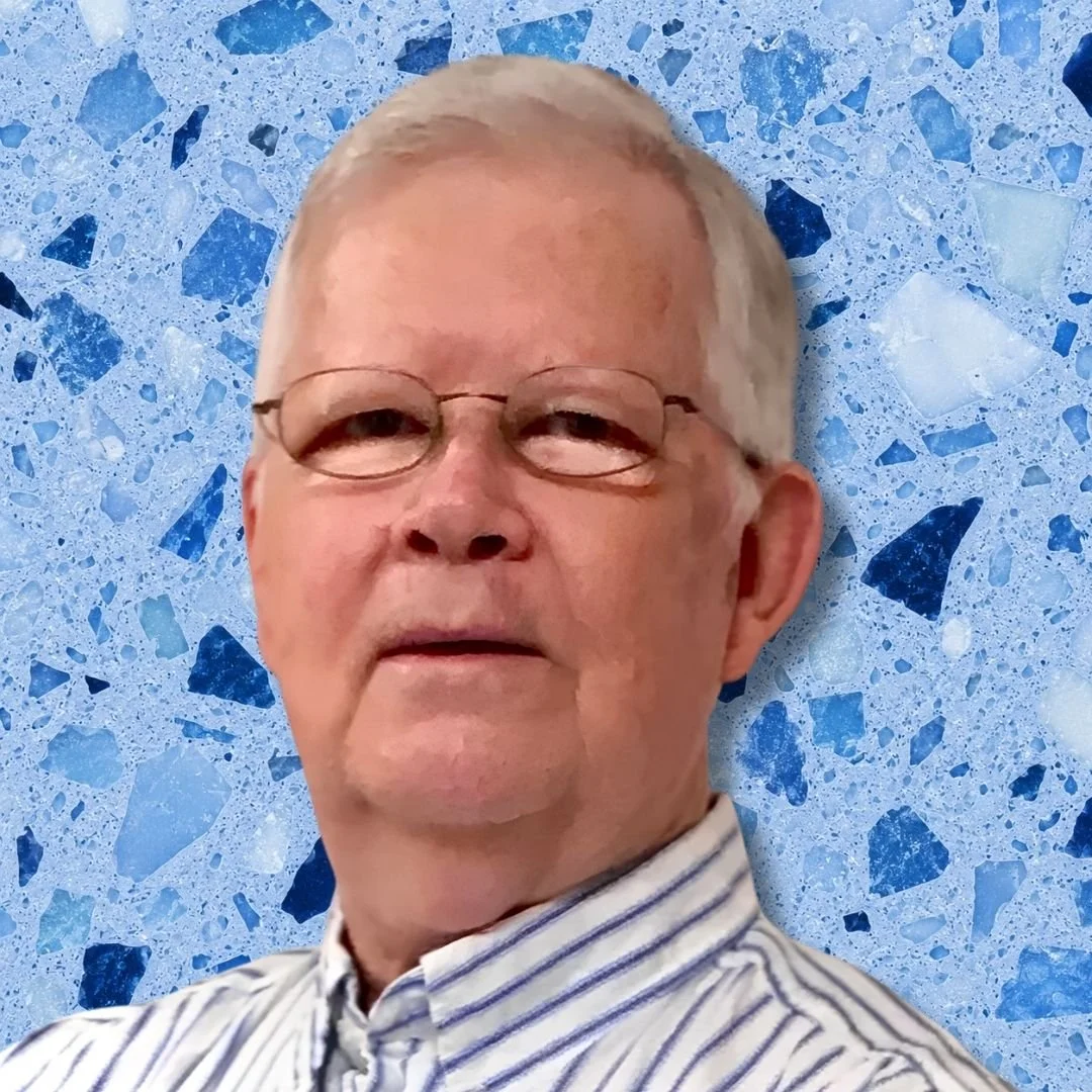A man with glasses and gray hair wearing a striped shirt in front of a blue terrazzo background.