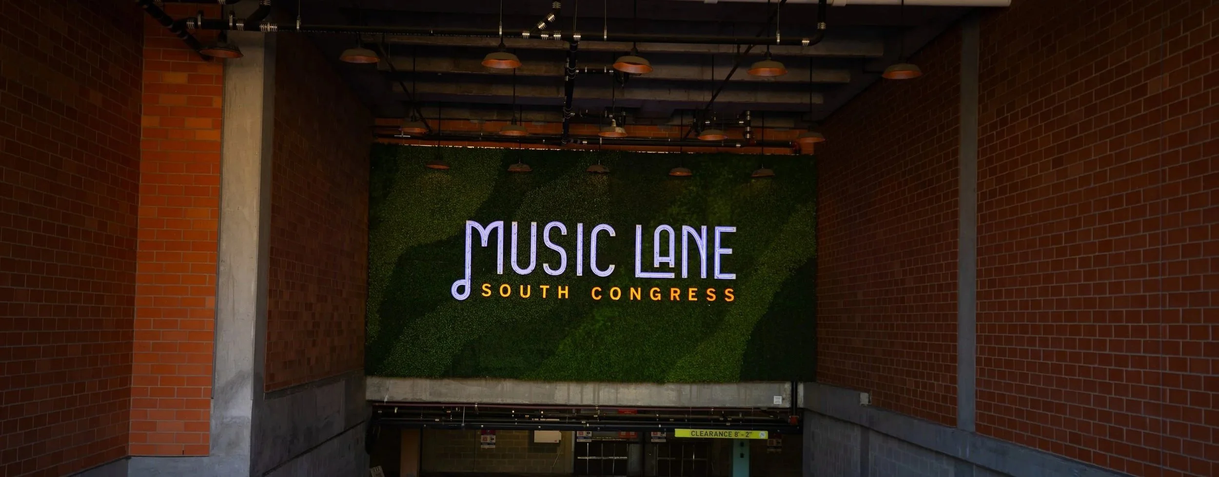 Sign that reads "Music Lane South Congress" against a green wall with brick walls on either side.