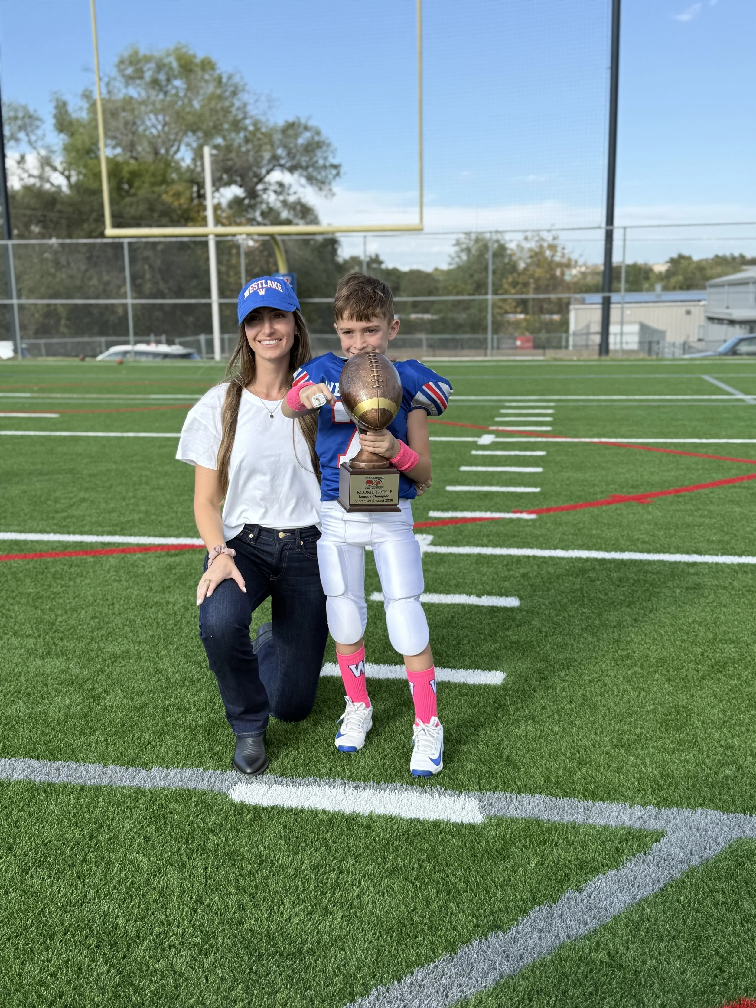 A woman kneeling next to a young football player holding a trophy on a football field.