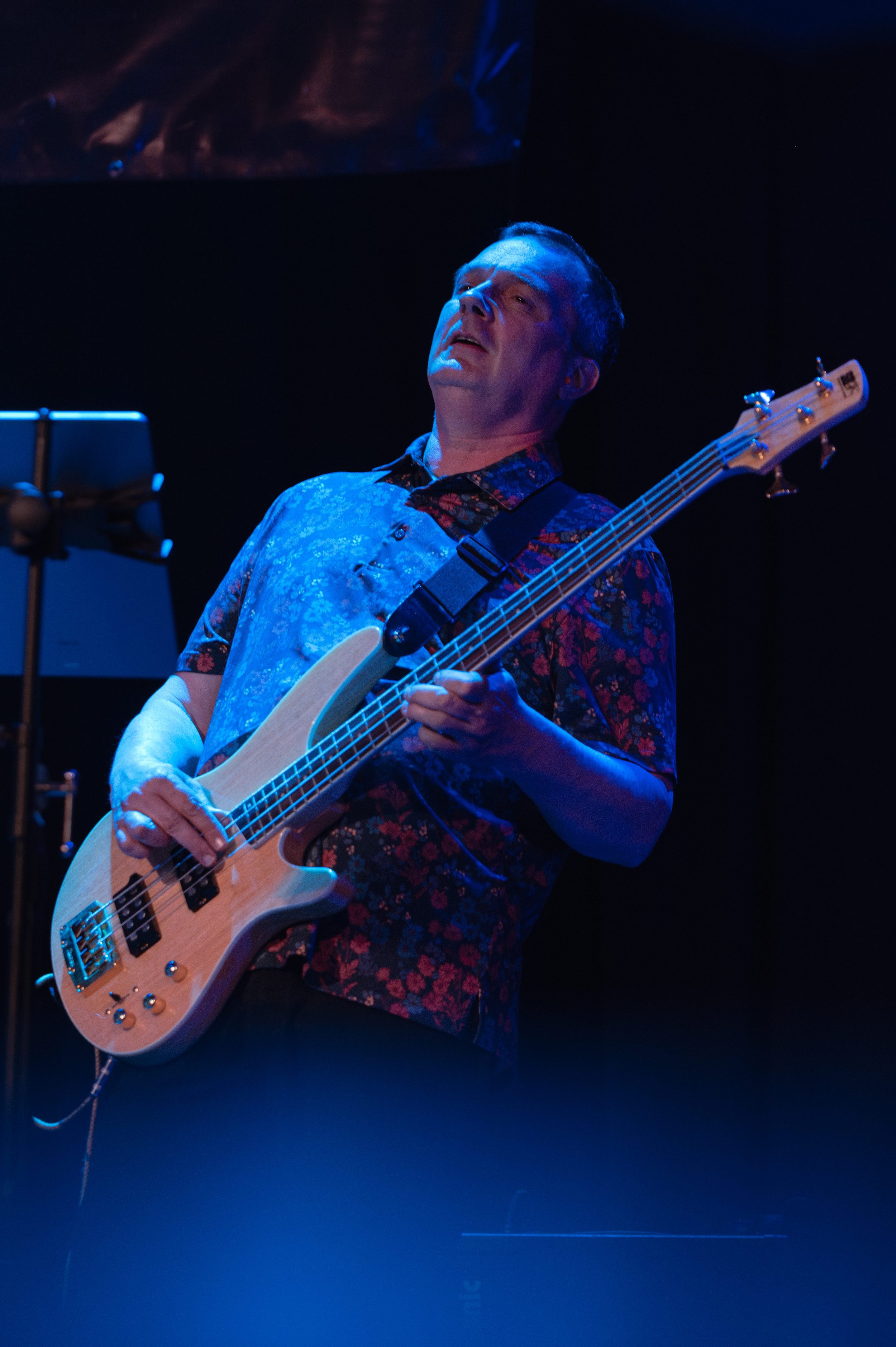 A man playing an electric bass guitar on stage, illuminated by blue stage lighting. Seraphina Soul playing live soul music at a Lancaster private celebration.