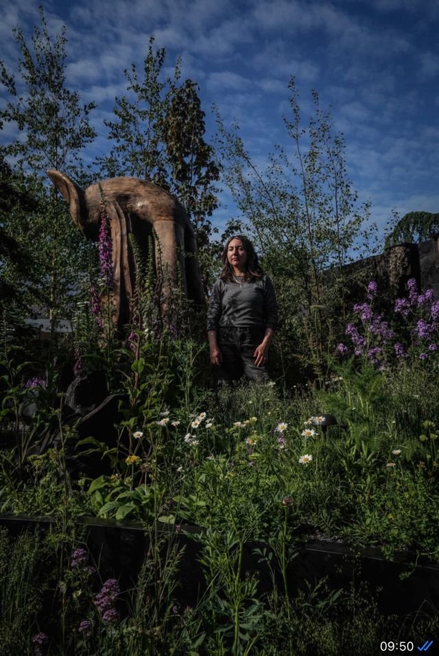 A picture of a dark haired garden designer Melanie Hick standing in twilight in the Nocturnal Garden at the Chelsea Flower Show 2026.