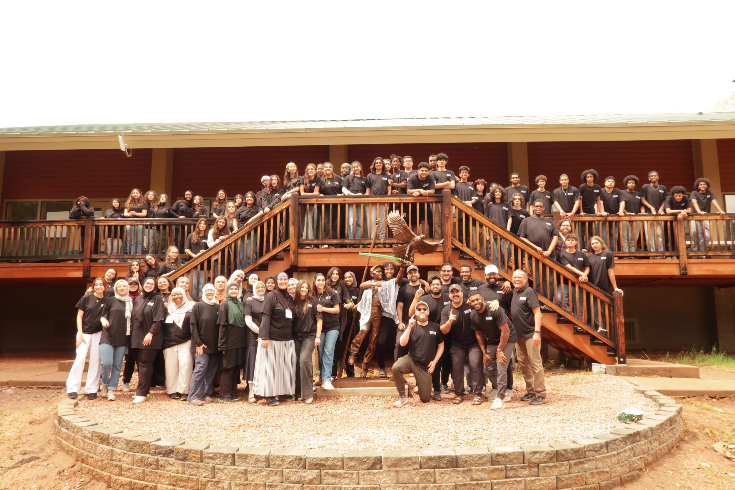 Large group of diverse people gathered on a wooden staircase and porch of a building, posing for a group photo outdoors.