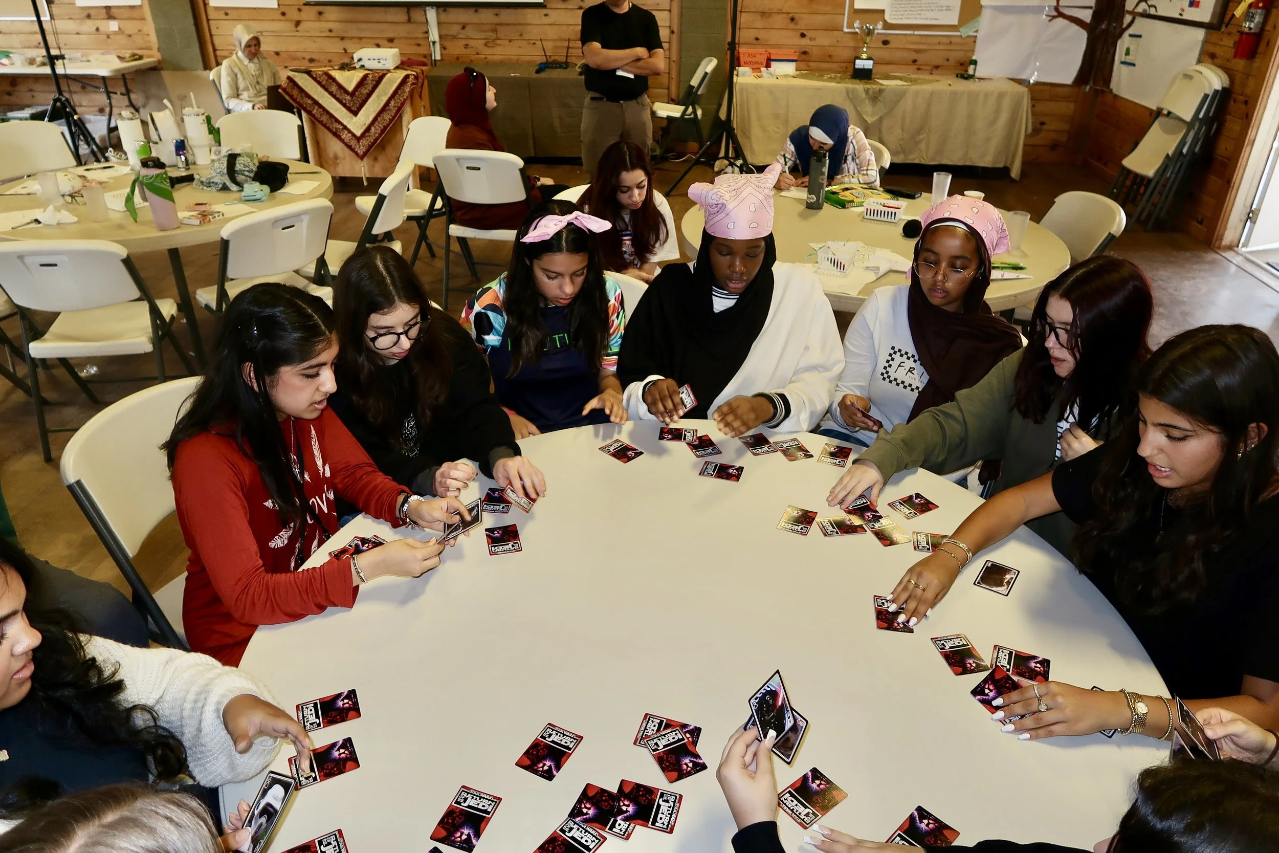 Group of young women sitting around a large round table playing a card game.