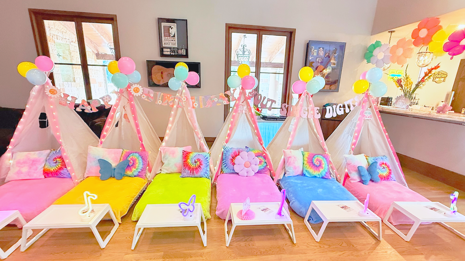 Colorful indoor birthday setup with five tents, tie-dye pillows, stuffed butterflies, and a balloon garland with pink, yellow, green, and purple balloons, celebrating a girl named Harper.