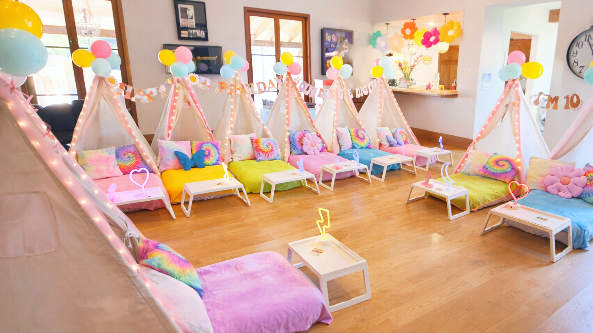 Colorful teepees and cushions set up for a children's birthday party in a living room, decorated with balloons, flowers, and string lights.