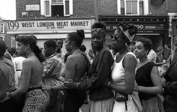 Young Black women along a crowded street, their posture attentive, West London, England (Portobello / Ladbroke Grove area), circa 1970s.