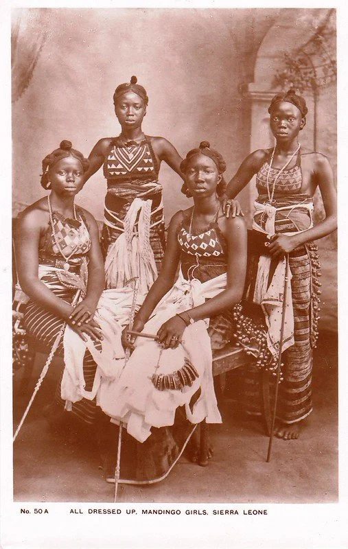 Traditional Mandingo (Mandinka) initiation attire, featuring handwoven country cloth wraps and geometric embroidered bodices, worn by young women in Sierra Leone around 1910. Photograph retrieved from Keir Dellar via Flickr.
