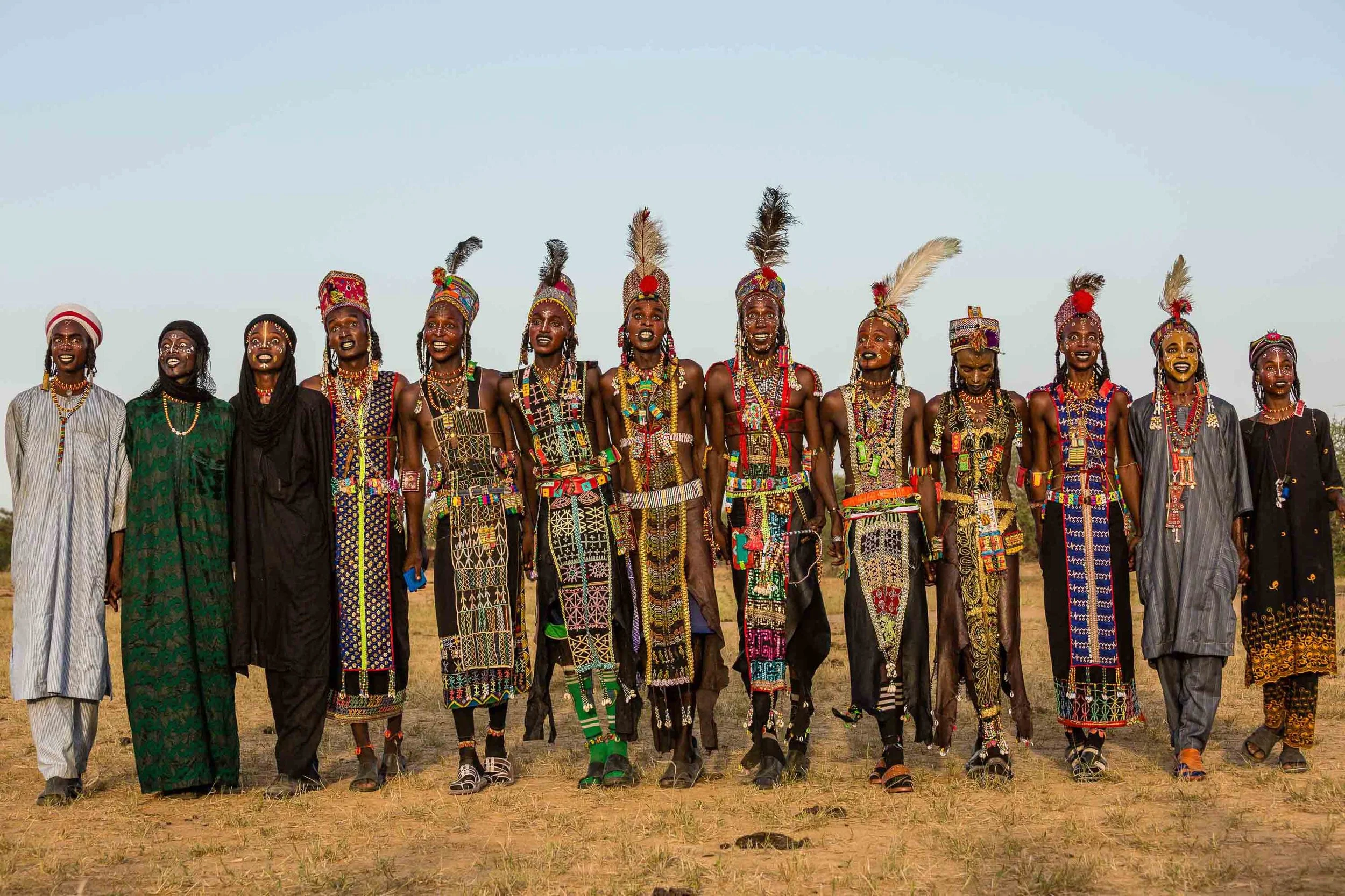 A long line of Wodaabe men and boys, wearing bejeweled leather tunics and sparkling crowns and feathers
Photo: Tariq Zaidi