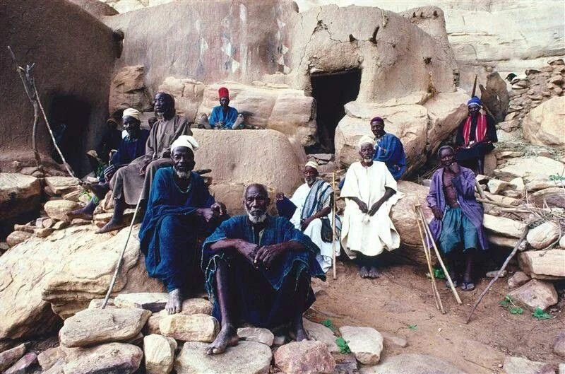 A group of Dogon men sitting outside cliffside dwellings in Mali.