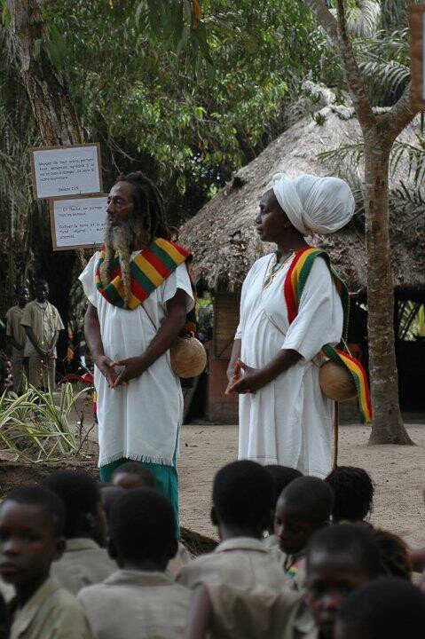 Rastafarian man and woman in white ceremonial garments with red, gold, and green sashes, attire commonly worn during Rastafarian gatherings and spiritual ceremonies.
