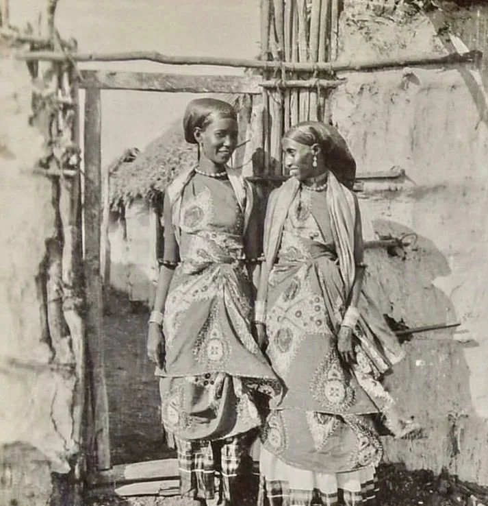 Two Somali women wearing a Guuntino (wrapped asymmetrical dress) on top of a pleated googorad (underskirt) and a garbasaar (headscarf on shoulders).