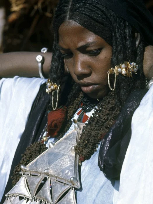 An Algerian woman wearing a pectoral pendant, serving as the focal point of a bride's adornment on her wedding day. Around her neck, she wears a collar made of cloves. Photographed by Maximilien Bruggmann in Illizi, Algeria, 1967. 