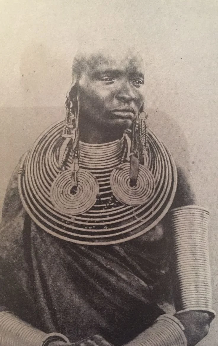 Maasai woman with brass neck coils and matching coiled earrings. These neck coils are traditionally worn to represent wealth, high social status, or a husband's affection. Photographer unknown.