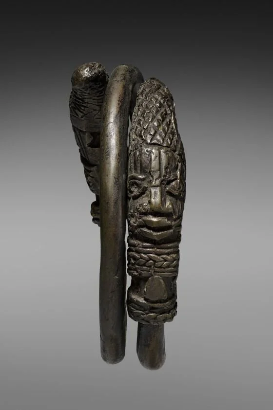 An 19th-century Benin hand coil from Nigeria, crafted from a copper alloy by Edo peoples royal brasscasters. It is designed as a ceremonial item to be grasped vertically by a chief during the annual Igu festival, rather than worn on the wrist.