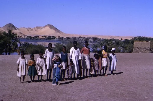 "Nubian youngsters, Sonqi." A image of a group of Nubian children standing in a desert village landscape. Emery, J. (Photographer). (Nubian youngsters, Sonqi). Flickr.  © James Emery. Licensed under the Creative Commons Attribution 2.0 Generic (CC BY