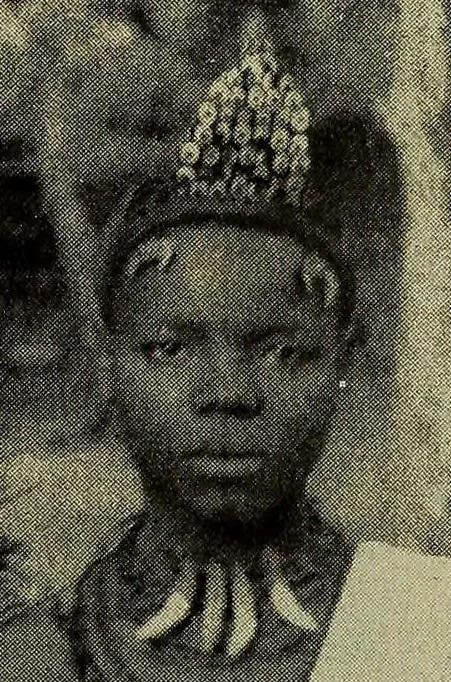 An Igbo woman wearing a necklace made of leopard's teeth mixed with aggry beads. These necklaces were strictly reserved for chiefs, nobility, and their prospective brides. They served as a direct visual marker of wealth, high social standing, and pol