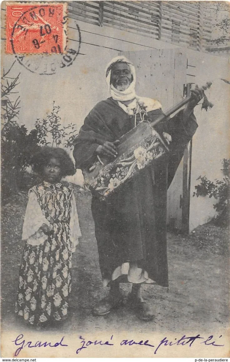 Gnawa musician playing a guembri next to child.