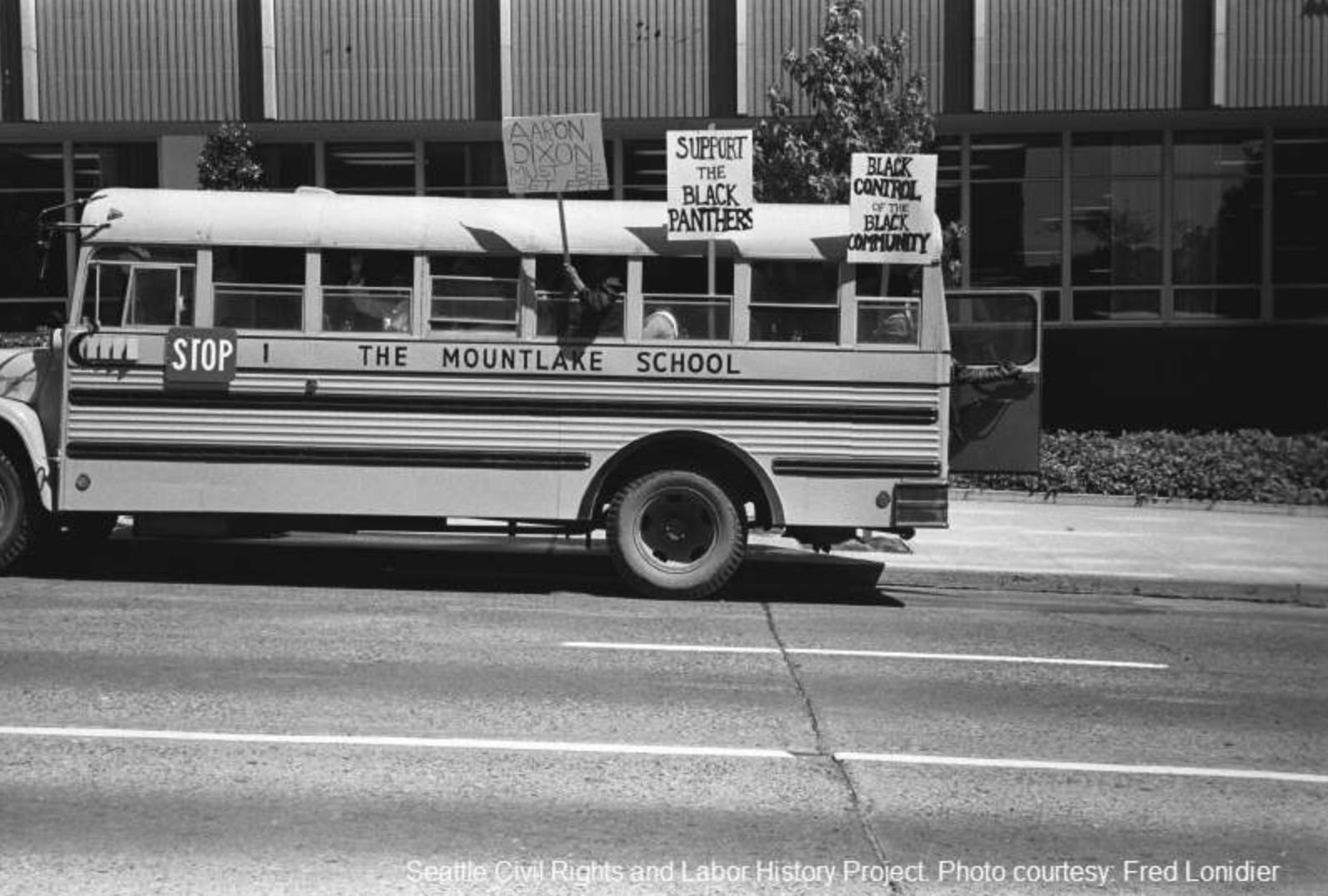 Photograph of a school bus carrying Black Panther Party supporters holding signs reading “Support the Black Panthers” and “Black control of the Black community.” Photographer Fred Lonidier, c. late 1960s to early 1970s. Seattle Civil Rights & Labor H
