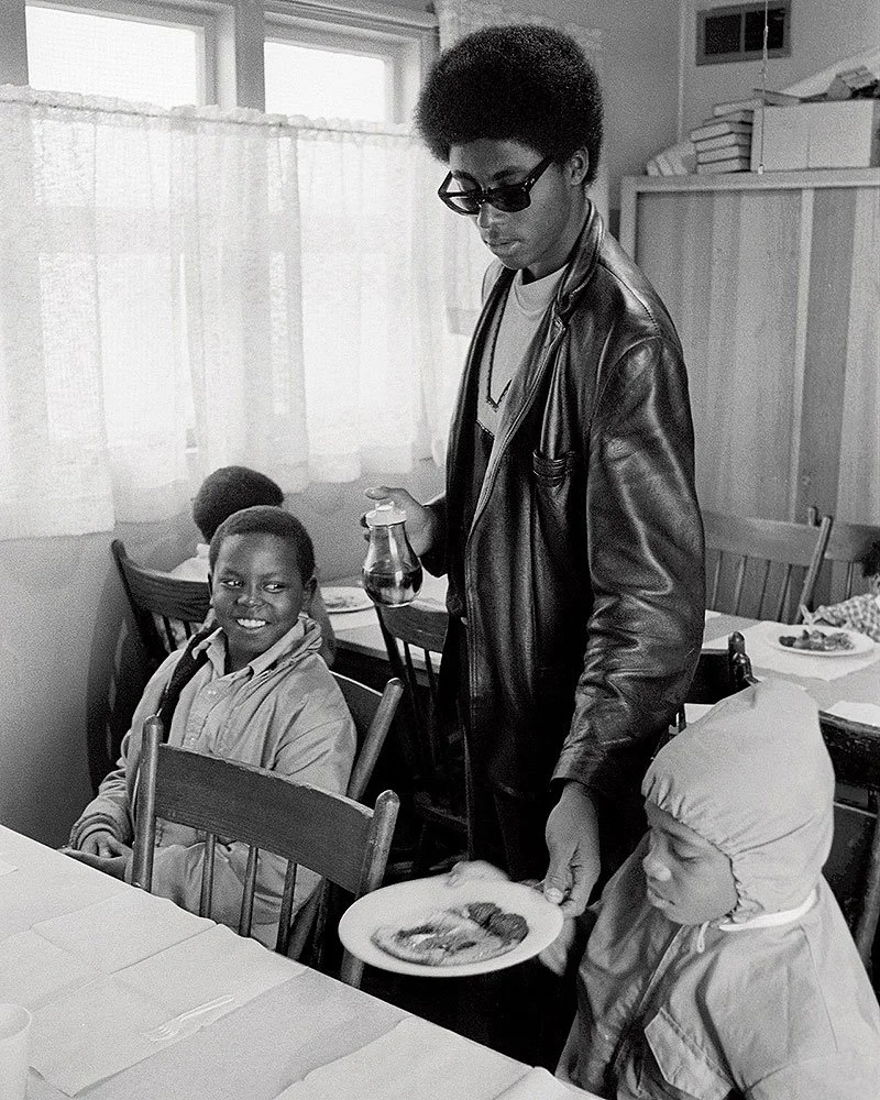 Photograph of a Black Panther Party member serving breakfast to children as part of the Free Breakfast for Children Program. Photographer unknown, c. late 1960s to early 1970s.