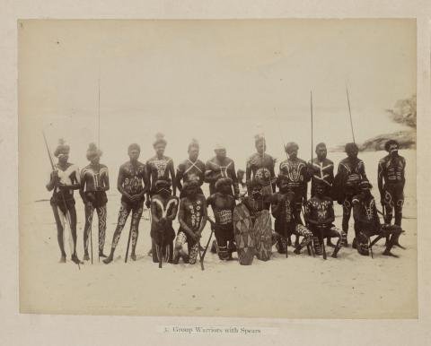 Image of a group of warriors with spears, posing on a beach.
