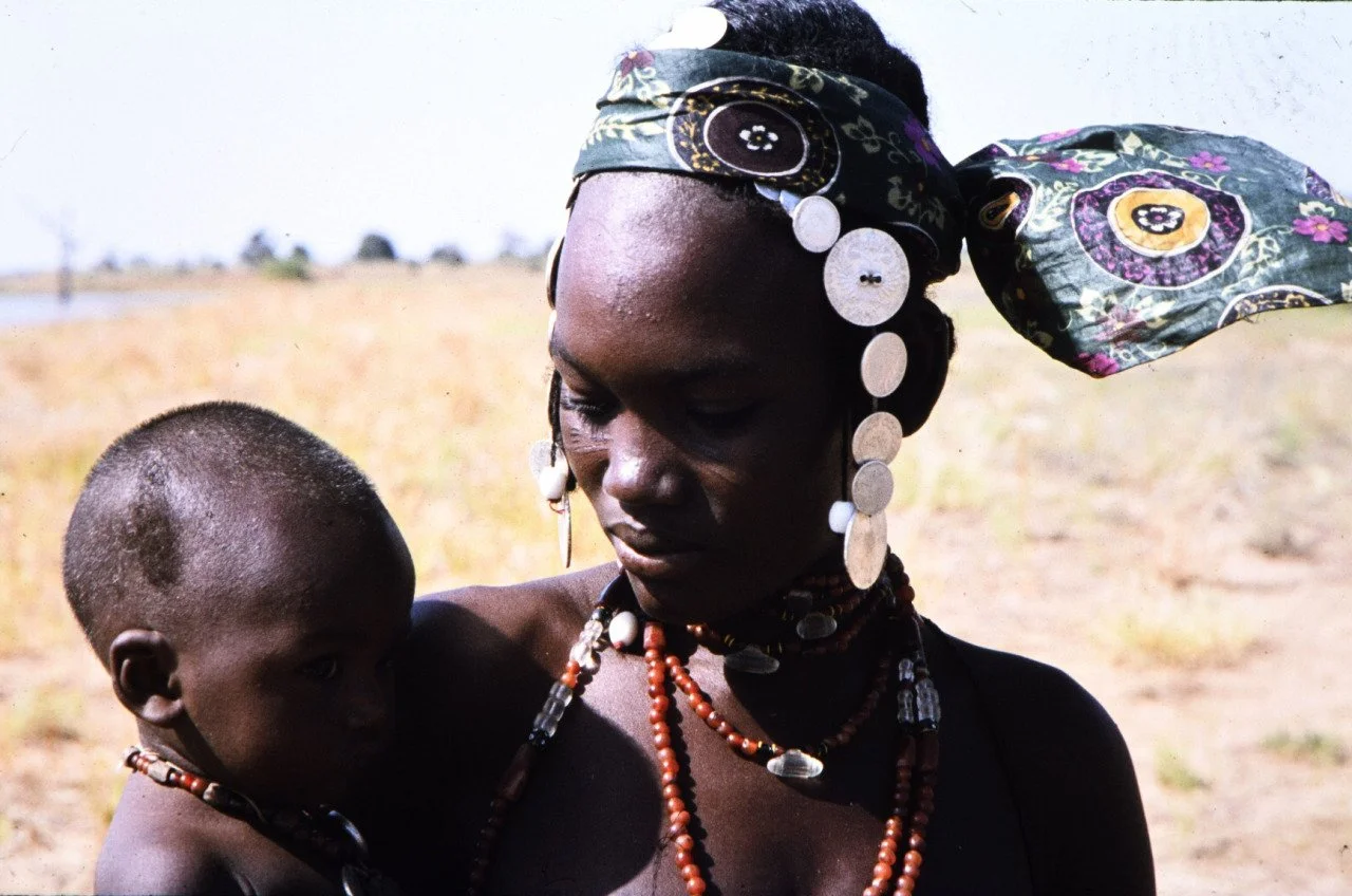Fulani woman wearing silver coins in her hair, which allows women to easily carry and protect family savings while moving across the Sahel region. Photographed by Johan Theodorus Broekhuijse in Burkina Faso, 1978.