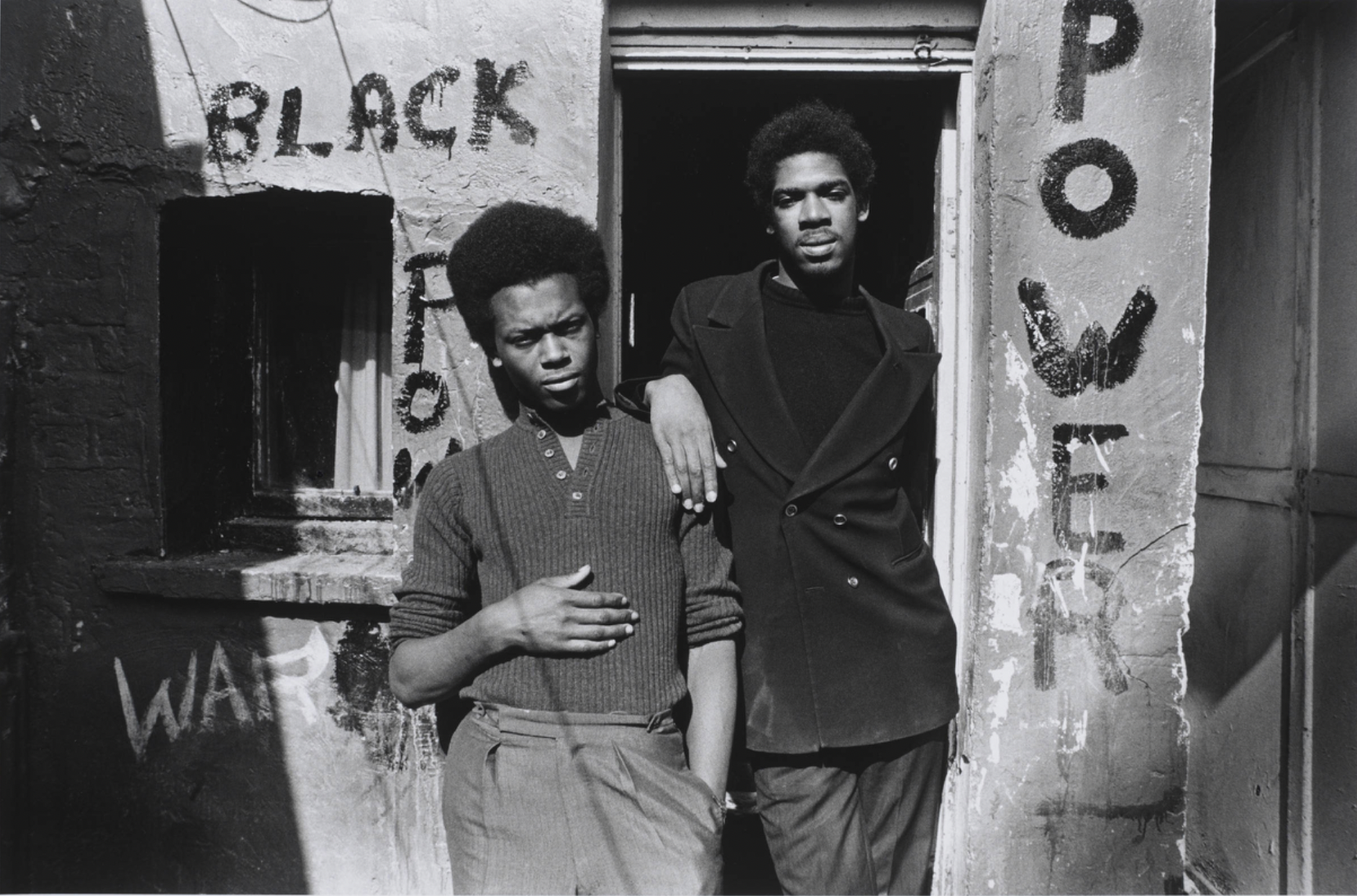Underside of overturned car with two men walking past from the series Handsworth Riots, photograph by Pogus Caesar, 1985, England. Museum no. E.1200-2012. © Pogus Caesar/ Victoria and Albert Museum, London.