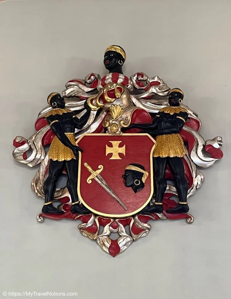Close up of the Coat of Arms of the Brotherhood of Blackheads. It shows the face of a Black man, a sword and a cross inside of a shield representing the patron of the brotherhood, Saint Maurice. By Diana Petterson, 2022.