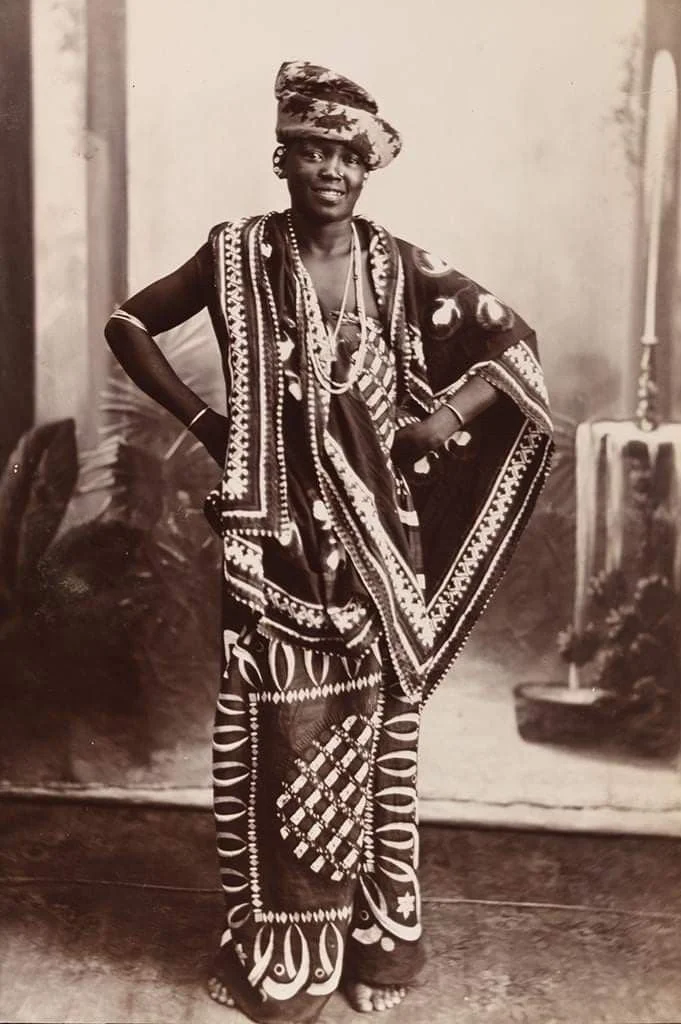 Traditional Kanga (or Leso) attire and a wrapped headscarf worn by a woman from the Kingdom of Zanzibar around 1900.